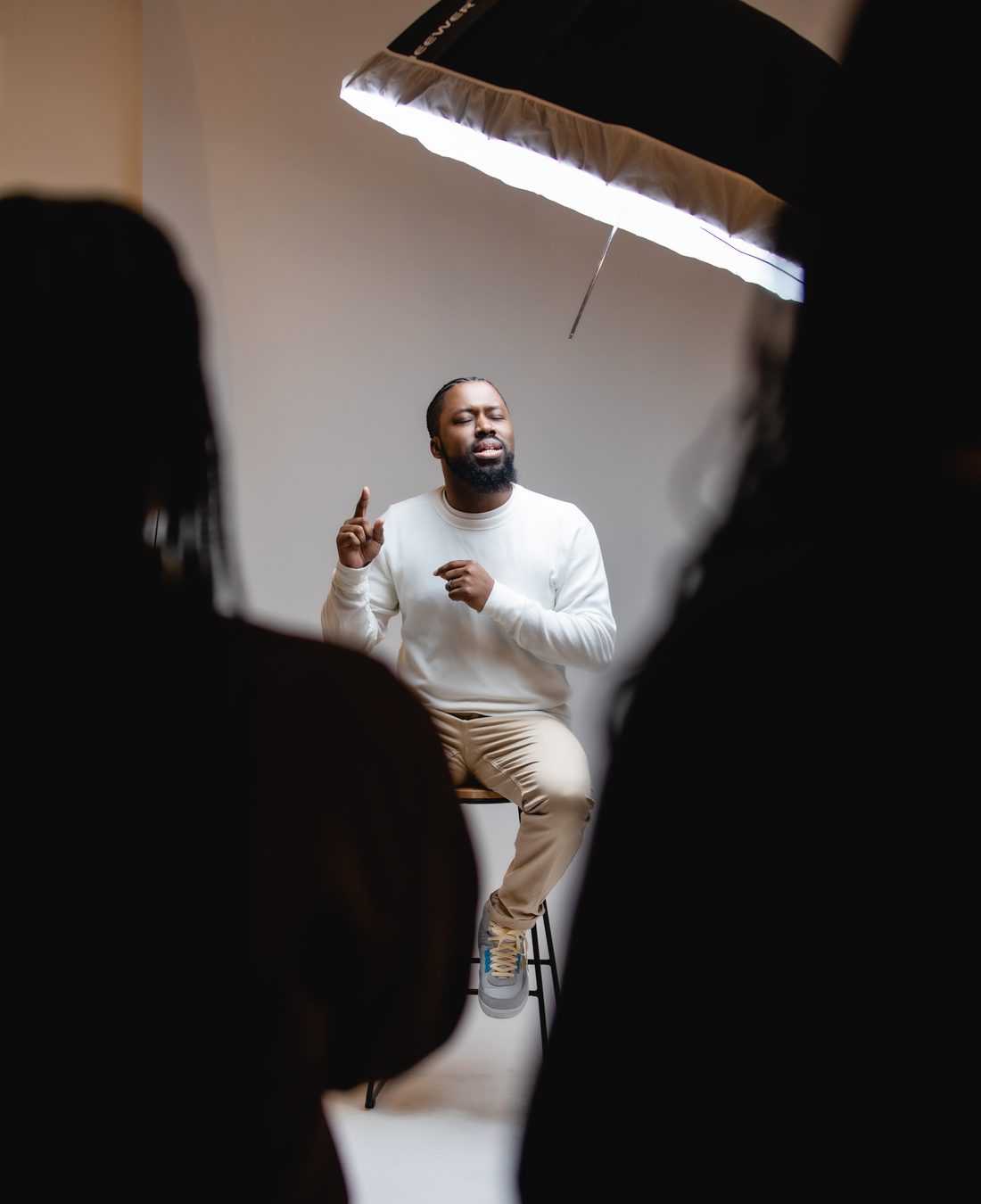 Romel Sylne Jr. seated on a stool, gesturing as he speaks to a small group in a softly lit studio